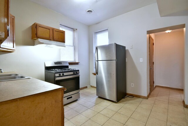 kitchen featuring range hood, brown cabinets, visible vents, appliances with stainless steel finishes, and a sink