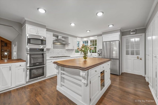 kitchen featuring wall chimney exhaust hood, stainless steel appliances, tasteful backsplash, wooden counters, and white cabinetry