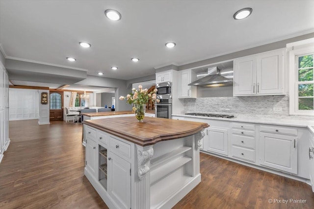 kitchen featuring a kitchen island, white cabinets, appliances with stainless steel finishes, and wall chimney exhaust hood