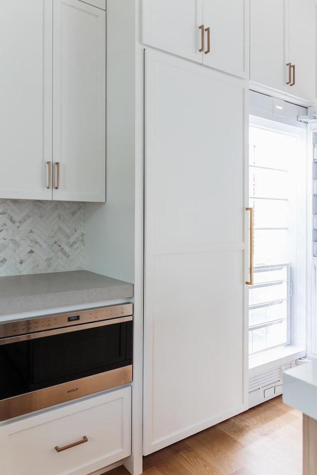 kitchen with tasteful backsplash, white cabinetry, and light hardwood / wood-style flooring