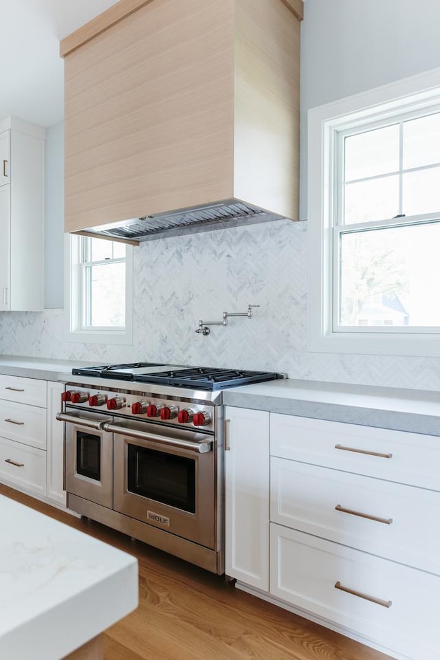 kitchen featuring white cabinets, wall chimney exhaust hood, double oven range, and tasteful backsplash