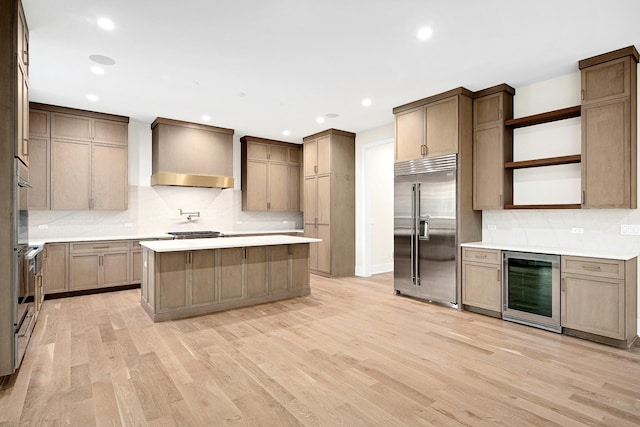 kitchen with a center island, beverage cooler, stainless steel appliances, wall chimney range hood, and light wood-type flooring