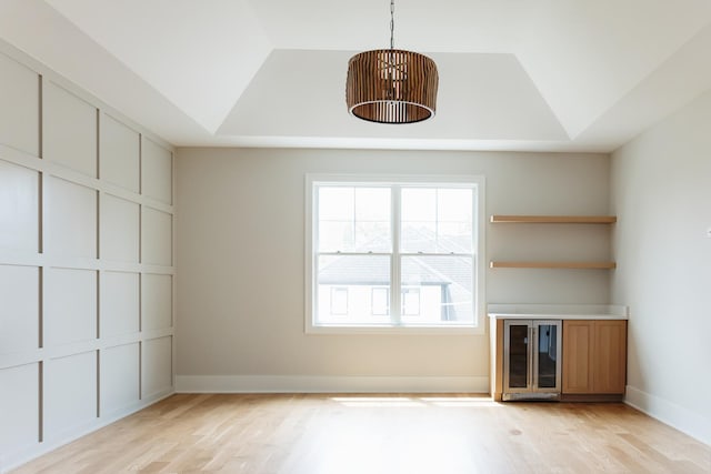 unfurnished living room featuring a raised ceiling, wine cooler, built in shelves, and light wood-type flooring