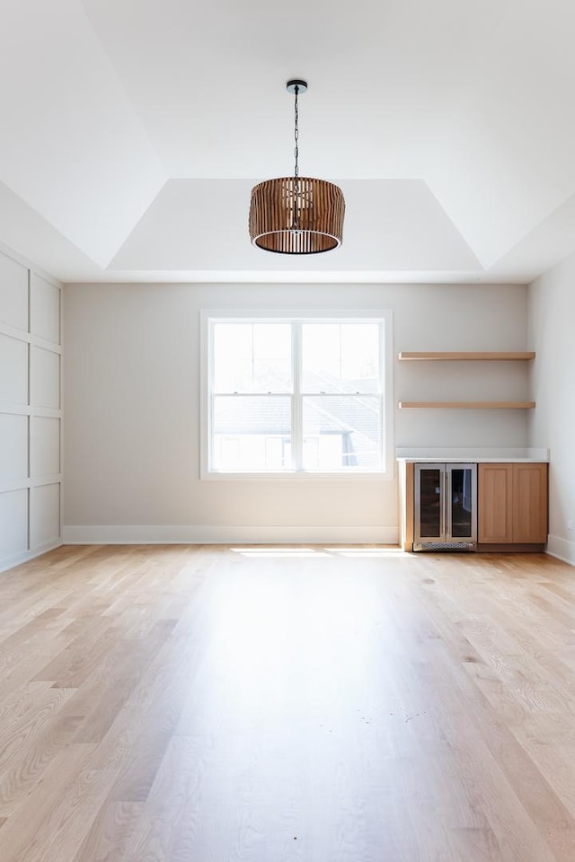 unfurnished living room with a tray ceiling, beverage cooler, and light hardwood / wood-style floors