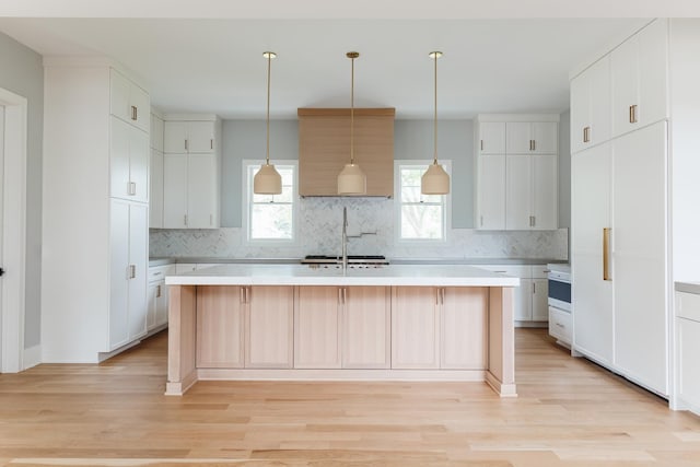 kitchen featuring backsplash, decorative light fixtures, a center island with sink, light hardwood / wood-style floors, and white cabinetry