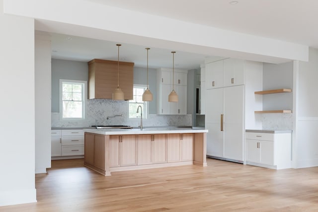 kitchen with a kitchen island with sink, white cabinets, hanging light fixtures, and light wood-type flooring