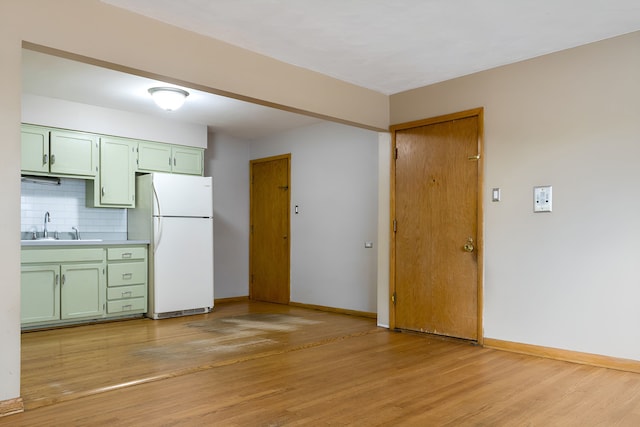 kitchen with white refrigerator, sink, tasteful backsplash, green cabinetry, and light hardwood / wood-style floors