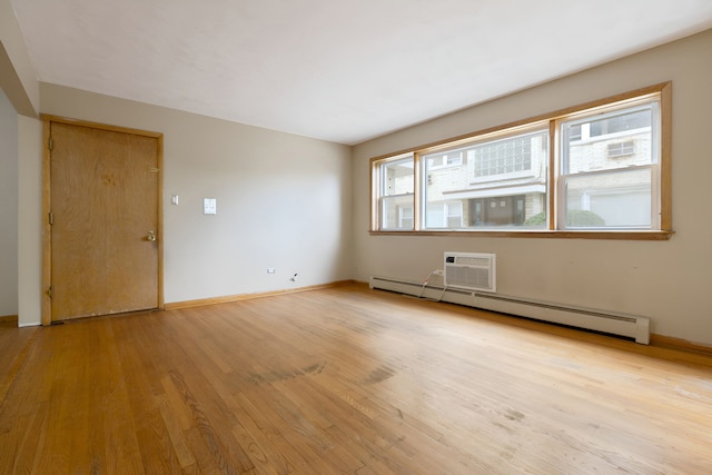 spare room featuring light wood-type flooring, a healthy amount of sunlight, a baseboard heating unit, and a wall mounted air conditioner