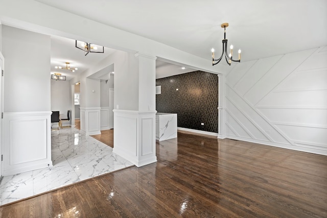 empty room featuring dark hardwood / wood-style flooring, a chandelier, and ornate columns