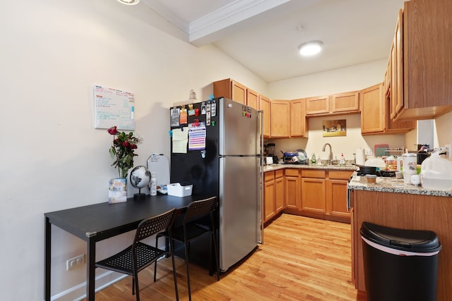 kitchen with light stone counters, sink, stainless steel refrigerator, crown molding, and light hardwood / wood-style floors