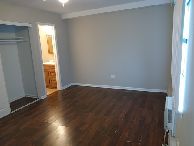 unfurnished bedroom featuring dark hardwood / wood-style floors, ensuite bath, a closet, and a wall unit AC