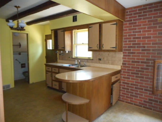 kitchen with backsplash, kitchen peninsula, brick wall, and sink