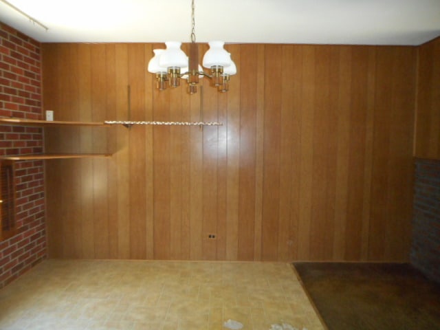 unfurnished dining area featuring wooden walls, a chandelier, and brick wall