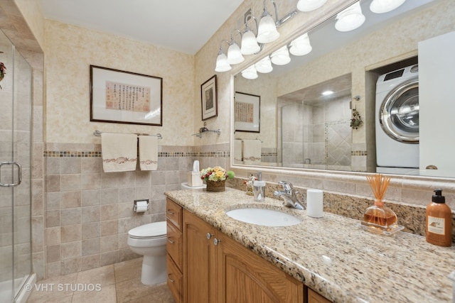 bathroom featuring tile patterned flooring, washer / clothes dryer, a shower with shower door, vanity, and tile walls