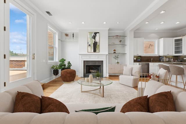 living room featuring a tiled fireplace, light hardwood / wood-style floors, a healthy amount of sunlight, and crown molding