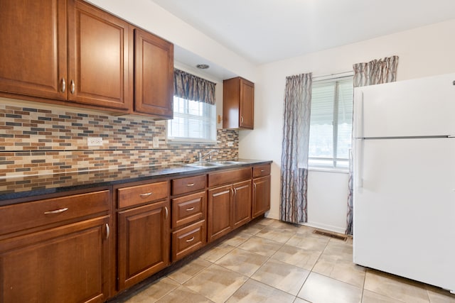 kitchen with light tile patterned floors, sink, dark stone counters, white fridge, and decorative backsplash