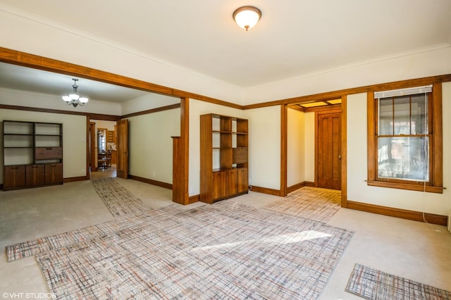 empty room featuring ornamental molding, light colored carpet, and an inviting chandelier