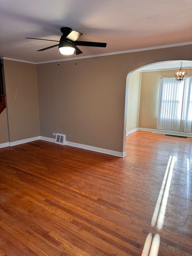 empty room with ceiling fan with notable chandelier, crown molding, and wood-type flooring