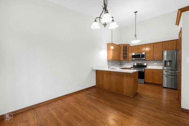 kitchen featuring dark hardwood / wood-style floors, sink, kitchen peninsula, stainless steel appliances, and decorative light fixtures