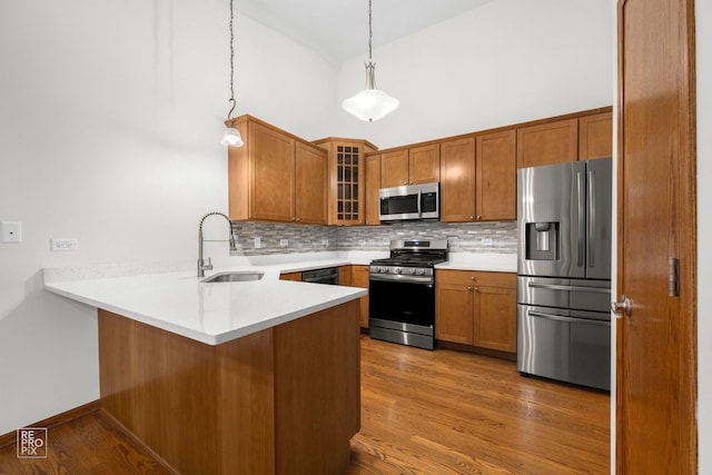 kitchen with light hardwood / wood-style floors, kitchen peninsula, appliances with stainless steel finishes, and hanging light fixtures