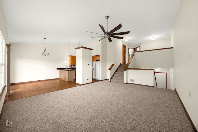 unfurnished living room featuring vaulted ceiling, ceiling fan with notable chandelier, and dark wood-type flooring