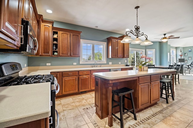 kitchen featuring a kitchen island, a breakfast bar, ceiling fan with notable chandelier, decorative light fixtures, and gas range oven