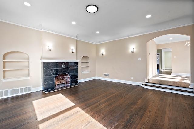 unfurnished living room featuring built in features, dark hardwood / wood-style floors, crown molding, and a tile fireplace