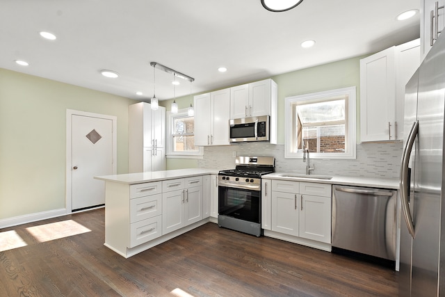 kitchen with sink, kitchen peninsula, decorative light fixtures, white cabinetry, and stainless steel appliances