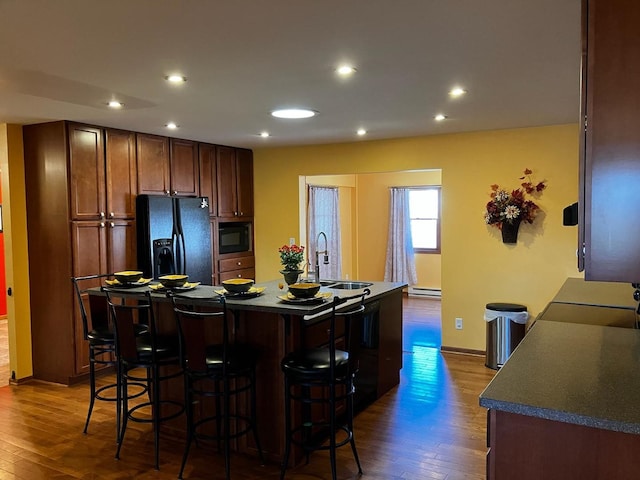 kitchen with baseboard heating, dark wood-type flooring, sink, an island with sink, and black appliances