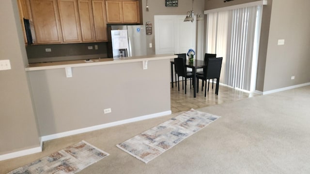 kitchen with pendant lighting, light carpet, a kitchen breakfast bar, stainless steel fridge, and a notable chandelier