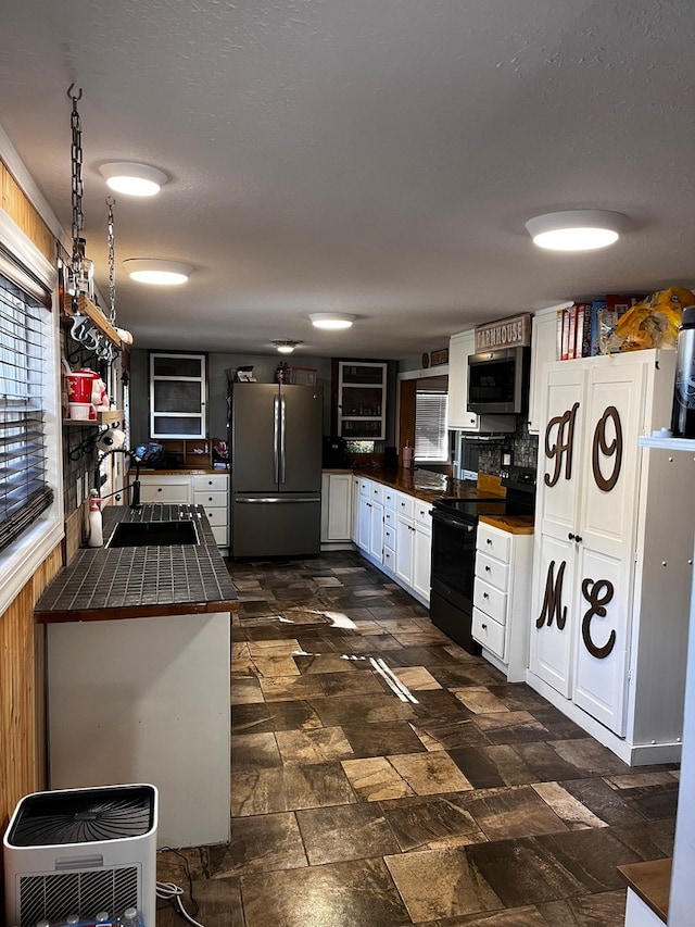 kitchen with sink, kitchen peninsula, white cabinetry, appliances with stainless steel finishes, and tile counters