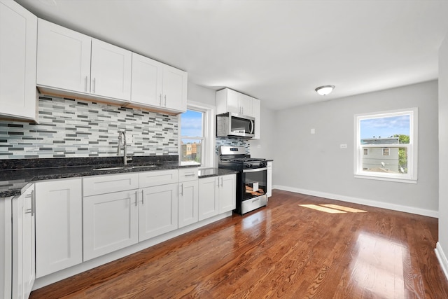 kitchen with white cabinetry, sink, appliances with stainless steel finishes, dark stone counters, and dark hardwood / wood-style floors