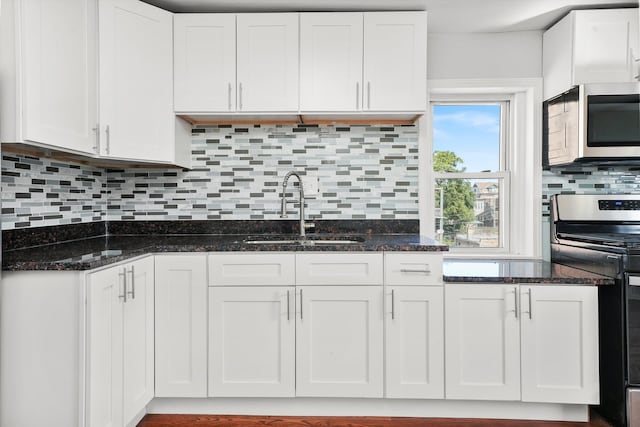 kitchen with stainless steel appliances, dark stone counters, white cabinetry, backsplash, and sink