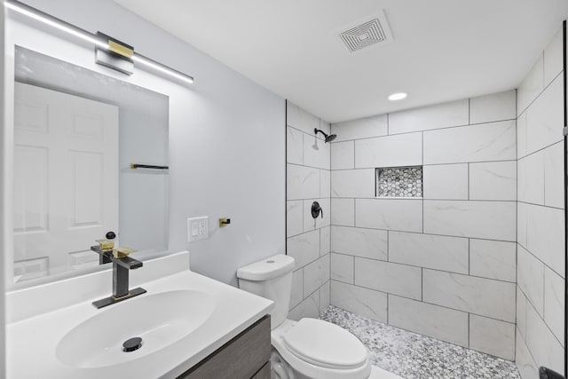 bathroom with tiled shower, vanity, and toilet