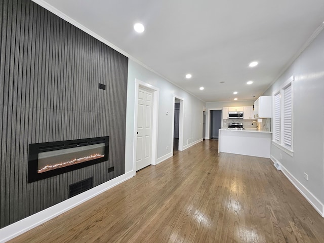 unfurnished living room featuring hardwood / wood-style flooring, sink, and crown molding