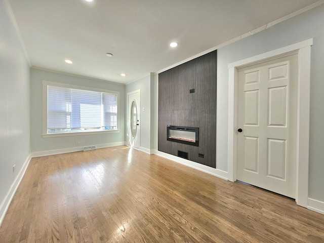 unfurnished living room with a large fireplace, crown molding, and light hardwood / wood-style flooring