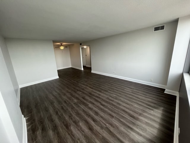 interior space featuring visible vents, a ceiling fan, baseboards, and dark wood-style floors