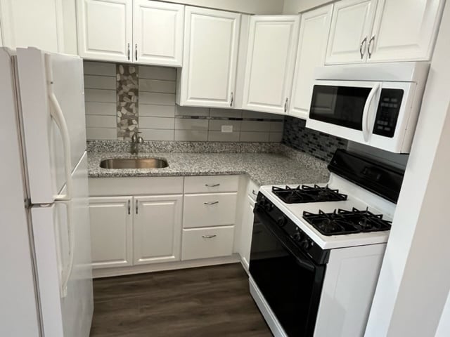 kitchen with decorative backsplash, dark wood-style flooring, a sink, white cabinets, and white appliances