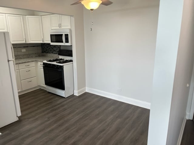 kitchen with white appliances, baseboards, dark wood-type flooring, white cabinets, and backsplash