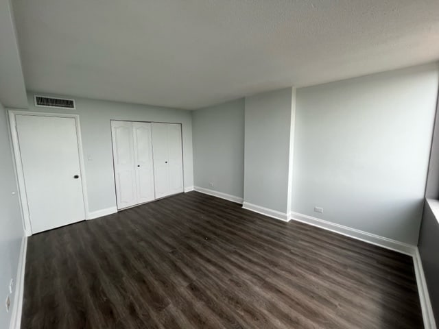 unfurnished bedroom with visible vents, baseboards, dark wood-style flooring, and a closet