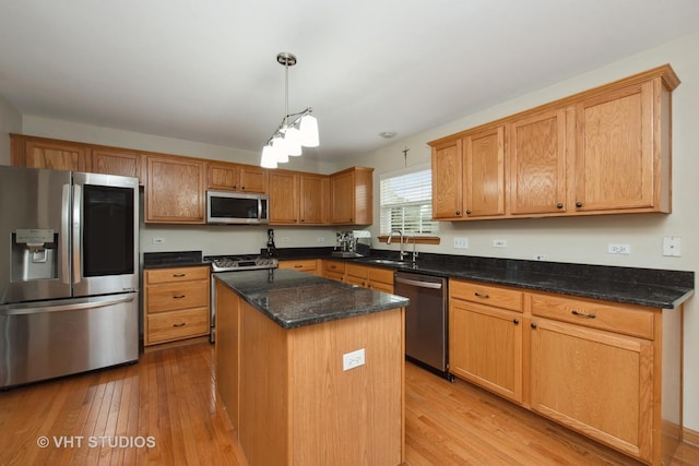 kitchen with dark stone countertops, light wood-type flooring, appliances with stainless steel finishes, decorative light fixtures, and a kitchen island