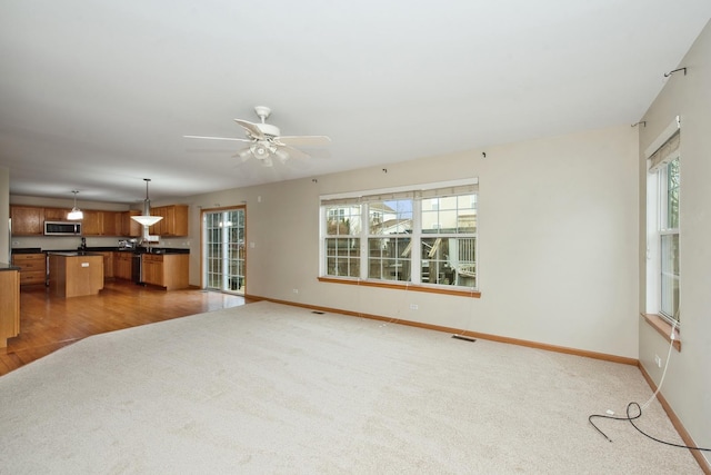 unfurnished living room with dark colored carpet, ceiling fan, and a wealth of natural light