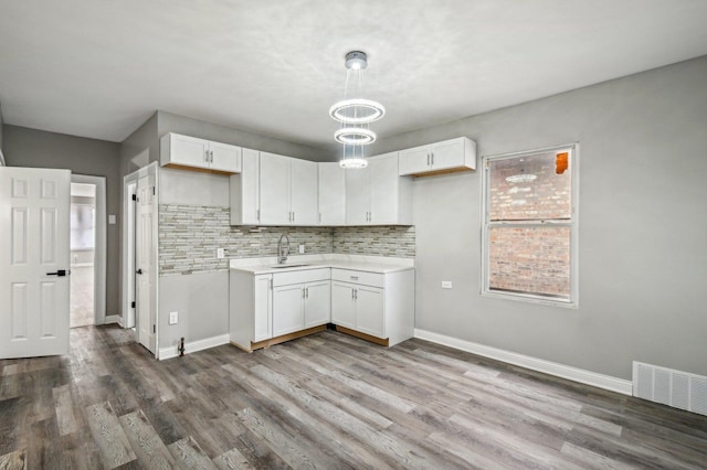 kitchen with backsplash, white cabinetry, sink, and wood-type flooring