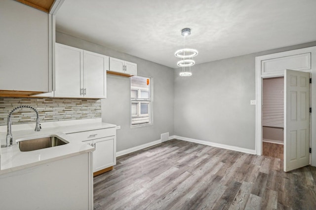 kitchen featuring backsplash, sink, light hardwood / wood-style floors, white cabinetry, and hanging light fixtures