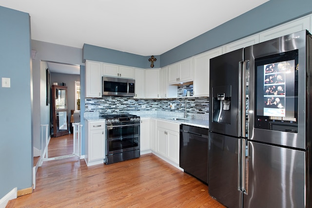 kitchen featuring white cabinets, sink, tasteful backsplash, stainless steel appliances, and light wood-type flooring