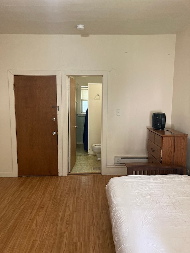 bedroom with connected bathroom, hardwood / wood-style floors, and a baseboard heating unit