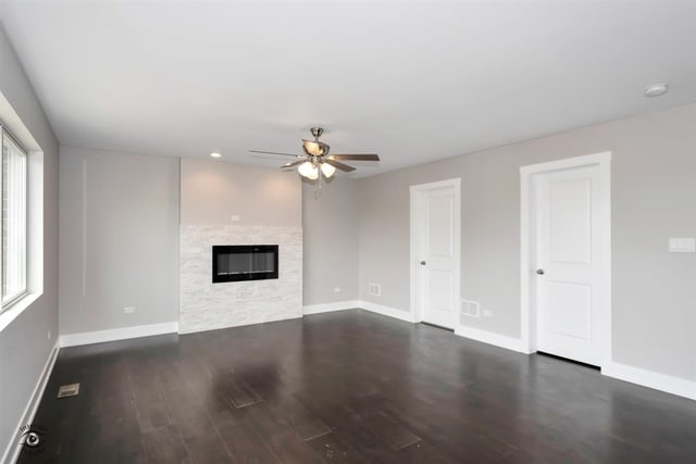 unfurnished living room featuring a stone fireplace, dark wood-type flooring, and ceiling fan