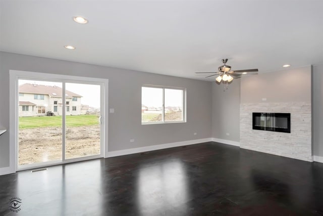 unfurnished living room featuring ceiling fan and a stone fireplace