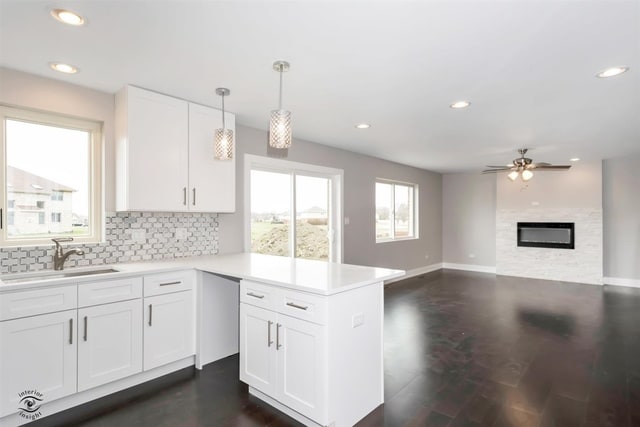 kitchen featuring pendant lighting, sink, white cabinetry, a fireplace, and ceiling fan