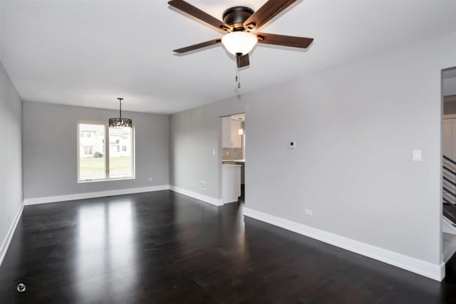 spare room with ceiling fan with notable chandelier and dark hardwood / wood-style flooring